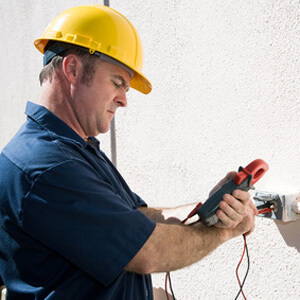 man in yellow hard hat wearing blue shirt looking at measuring device plugged into wall